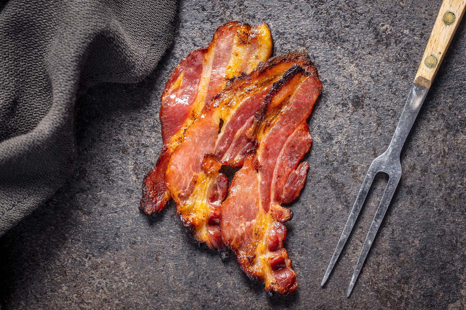 Bacon sliced and cooked on a table next to a fork