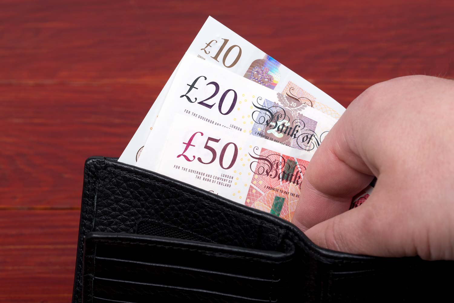 Hand opening a black wallet containing british bank notes