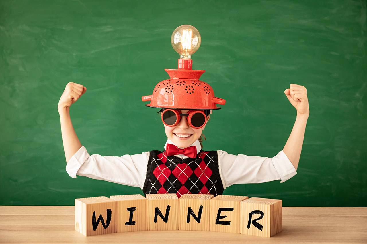 Competition winner concept - child with winner in wooden blocks, showing muscles, with a funny red hat